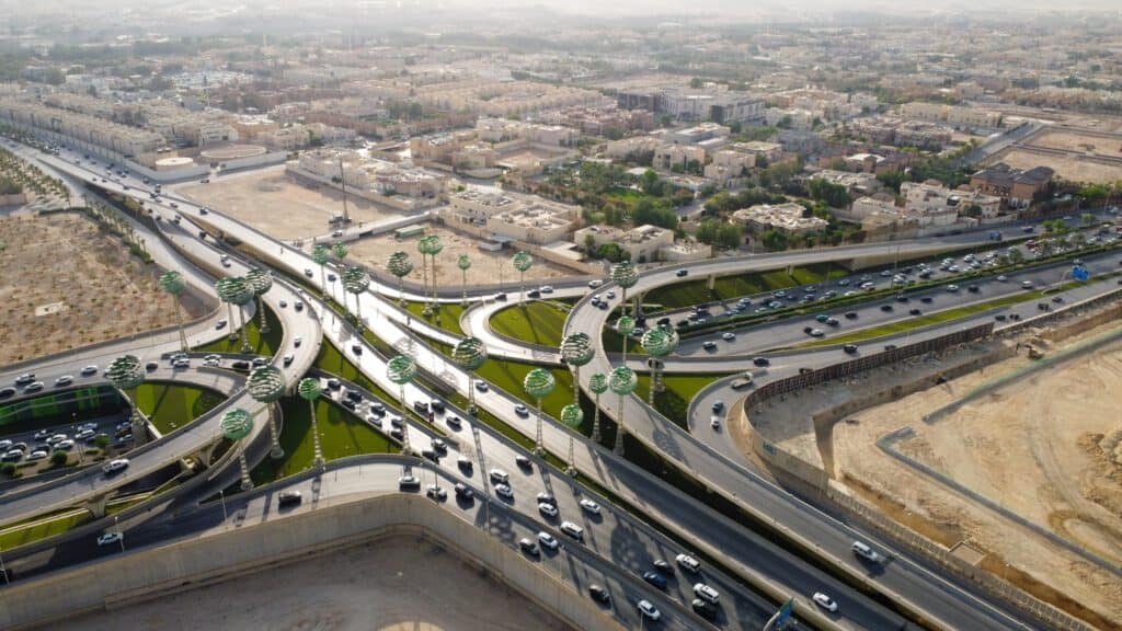 Highway interchange with green spherical art installations, roads, and surrounding urban landscape in a desert city.