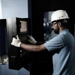 3 Industrial control panel operator working on automated machinery at a manufacturing facility.